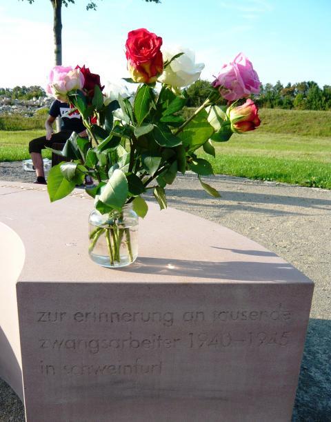 Acht Rosen auf derrosafarbenen Gedenk-Steinbank