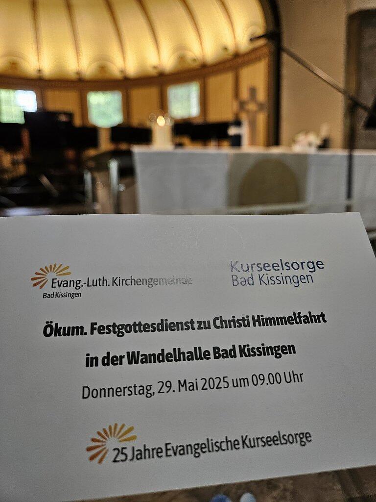 Das Liedblatt zum Gottesdienst vor einem verschwommenen Kreuz und dem erleuchteten Rund der Wandelhalle im Hintergrund