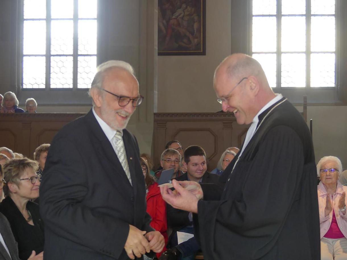 Dekan Oliver Bruckmann (rechts) ehrt den langjährigen Chorleiter Wolfhart Berger (links) mit einer seltenen Gedenkmünze von St. Johannis.
