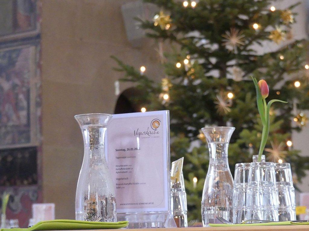Gedeckter Tisch mit Speisekarte, im Hintergrund der Weihnachtsbaum
