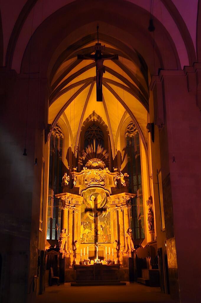 Das kleine Altarkreuz von St. Johannis Schweinfurt wirft in der weitgehend dunklen Kirche einen großen Kreuzschatten auf das Altarbild dahinter