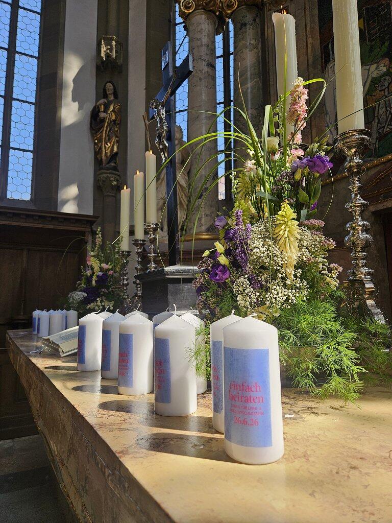 Viele Kerzen mit dem "Einfach heiraten" Logo stehen auf dem blumengeschmückten Altar