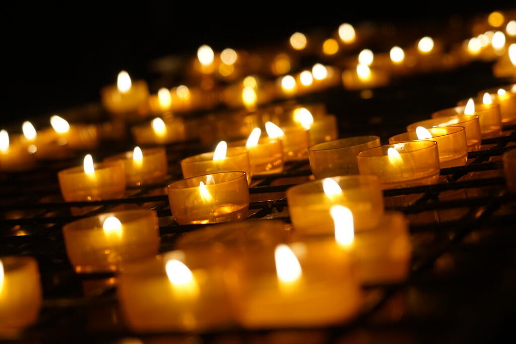 Brennende Kerzen vor dunklem Hintergrund. Etliche brennende Kerzen sind im Bild zu sehen. Die Kerzen im Vorder- und Hintergrund verlaufen in der Unschärfe.