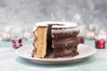 Foto von einem angeschnittenen Baumkuchen, mit Puderzucker bestreut, im Hintergrund glitzert es weihnachtlich-weiß mit angedeuteten Geschenkpaketen