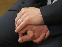 Nahaufnahme der ineinander gefalteten Hände eines Hochzeitspaars. Eine weitere Hand legt sich segnend darüber.