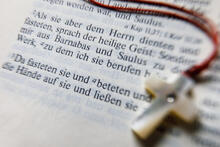 eine aufgeschlagene Bibel. Ein Bibeltext über das Fasten ist lesbar. Darüber liegt eine Kette mit einem Holzkreuz.
