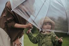 eine Mutter hält einen durchsichtigen Regenschirm über ihr Kind