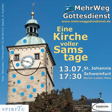 Der Turm der St. Johanniskirche Schweinfurt vor blauem Himmel. Die Kirchturmuhr sieht aus wie eine Nase zwischen den zwei Fenstern als Augen. Darunter ist mit einem Strich ein Mund angedeutet. Die Kirche ist übersät mit kleinen blauen Punkten.