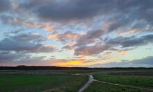 Ein Sonnenaufgang nach stürmischer Nacht vor Wolken. Im Vordergrund ein Feldweg.