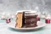 Foto von einem angeschnittenen Baumkuchen, mit Puderzucker bestreut, im Hintergrund glitzert es weihnachtlich-weiß mit angedeuteten Geschenkpaketen