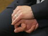 Nahaufnahme der ineinander gefalteten Hände eines Hochzeitspaars. Eine weitere Hand legt sich segnend darüber.