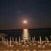 Der Mond scheint über dem Meer. Im Vordergrund am Strand Liegestühle, kein Mensch zu sehen.