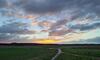 Ein Sonnenaufgang nach stürmischer Nacht vor Wolken. Im Vordergrund ein Feldweg.