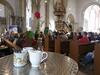 In der Vesperkirche Schweinfurt stehen Milchkännchen und Tische bereit. Die Menschen sitzen noch zum Gottesdienst in den Bänken.